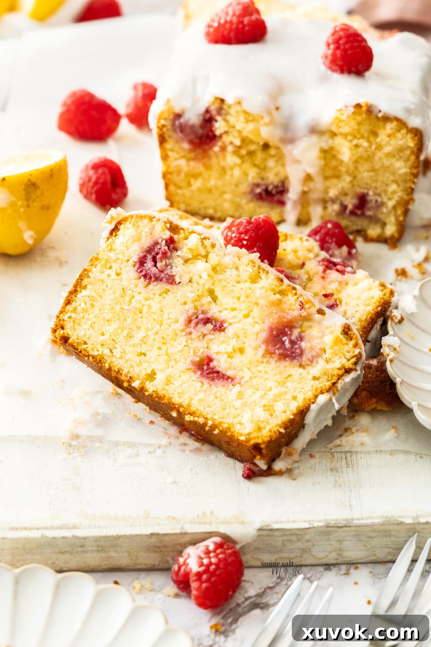A beautiful close-up of a slice of raspberry lemon loaf cake, showcasing its vibrant raspberry studs, moist crumb, and a generous drizzle of lemon glaze, inviting a bite.