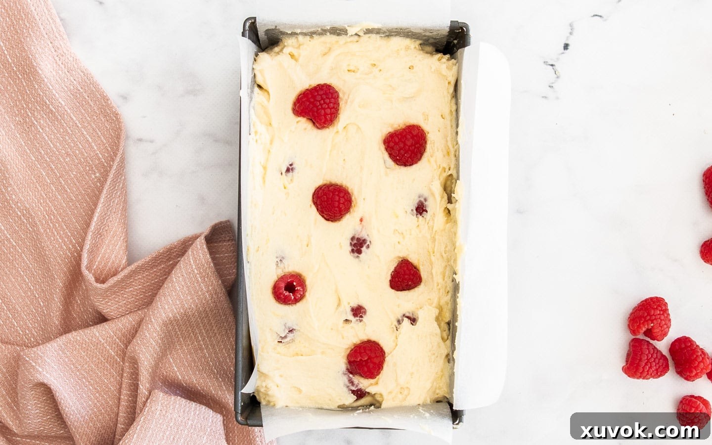 The layered cake batter in the loaf pan, topped with a final scattering of fresh raspberries, ready to be placed in the oven for baking.