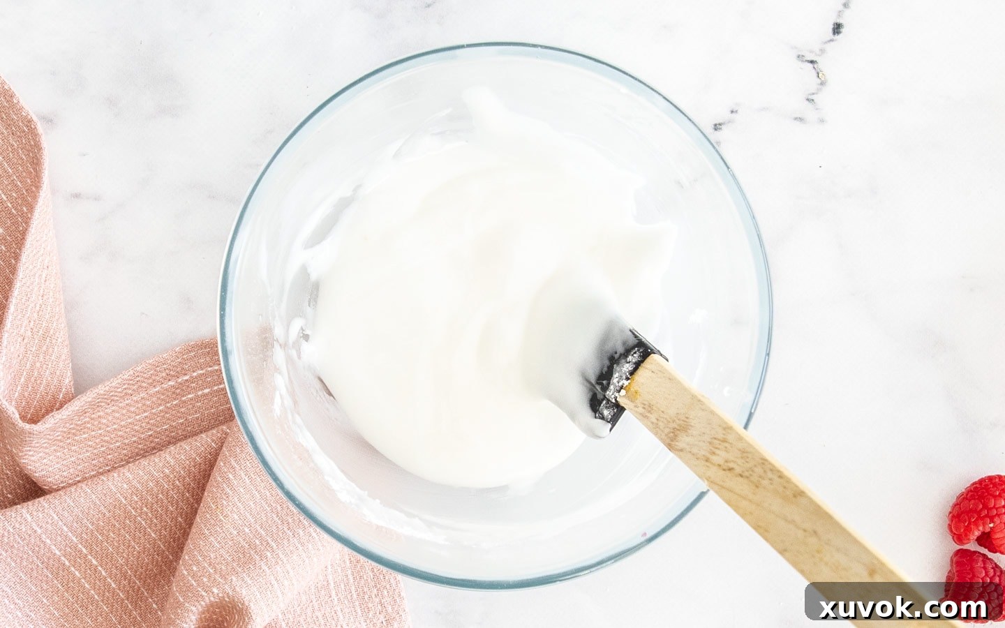 A bowl filled with freshly made, smooth, and glossy lemon icing, prepared to be drizzled over the cooled raspberry lemon loaf cake.