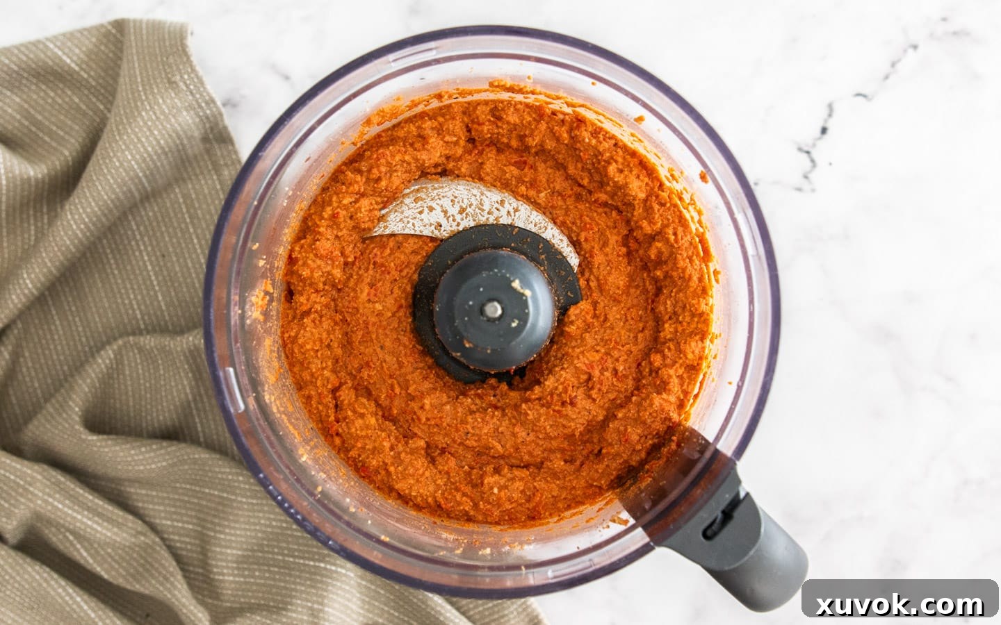 The blended romesco sauce ingredients in a food processor bowl before olive oil is added, showing a thick, coarse texture.