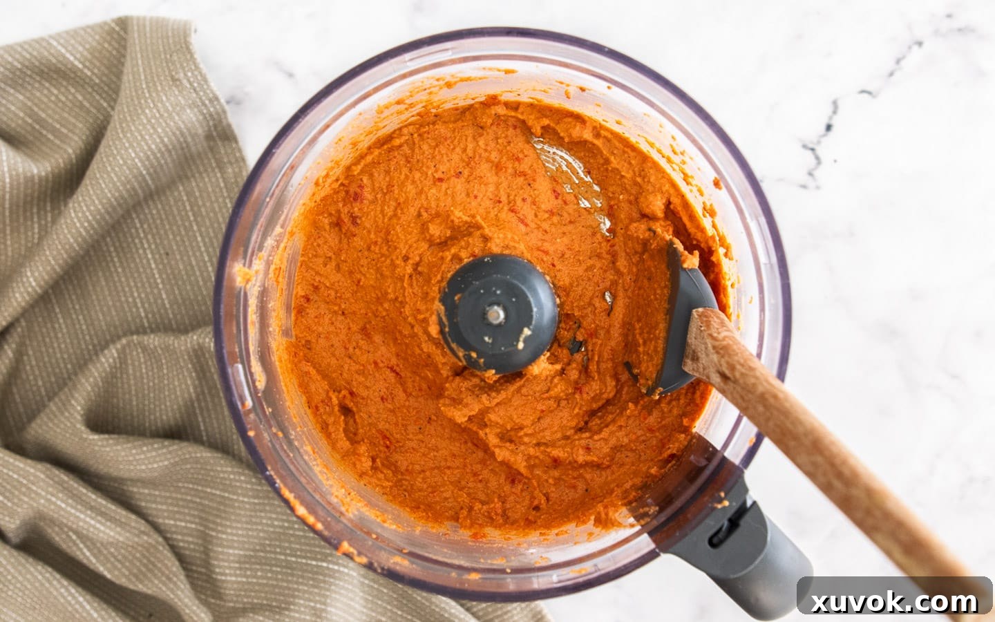 The romesco sauce being blended with olive oil in a food processor, transforming into a smoother, dip-like consistency.