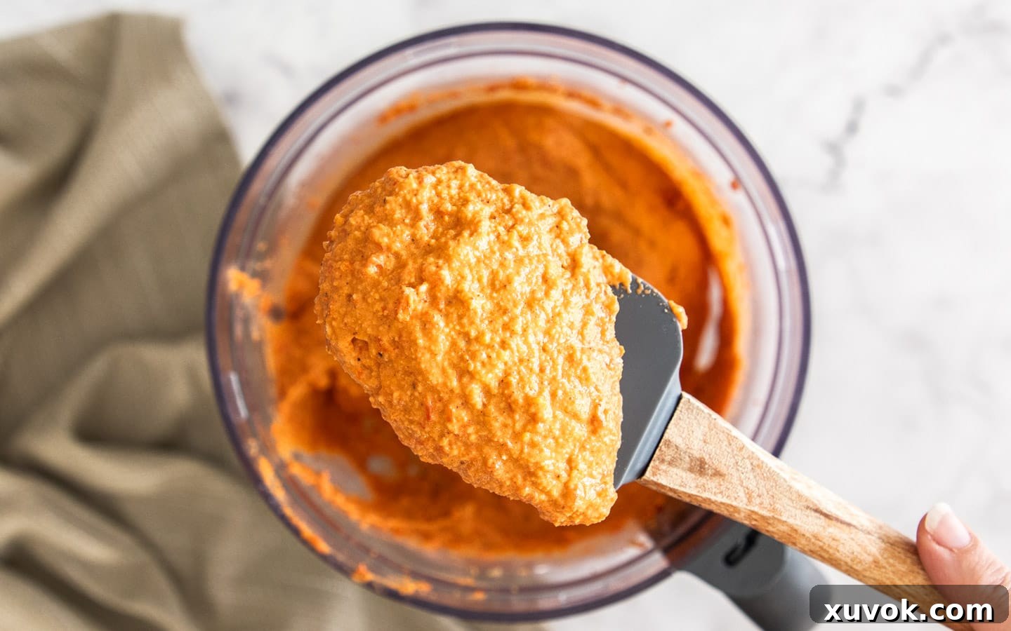 A spatula scooping the finished, creamy Romesco sauce, highlighting its vibrant color and smooth texture.