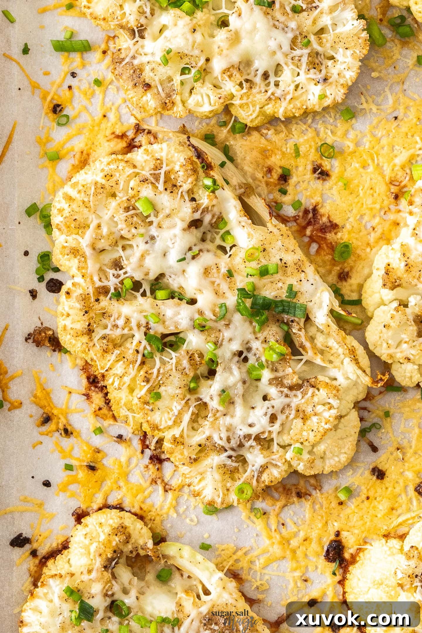 Closeup of a cheesy cauliflower steak, perfectly roasted and topped with melted cheese and fresh chives.