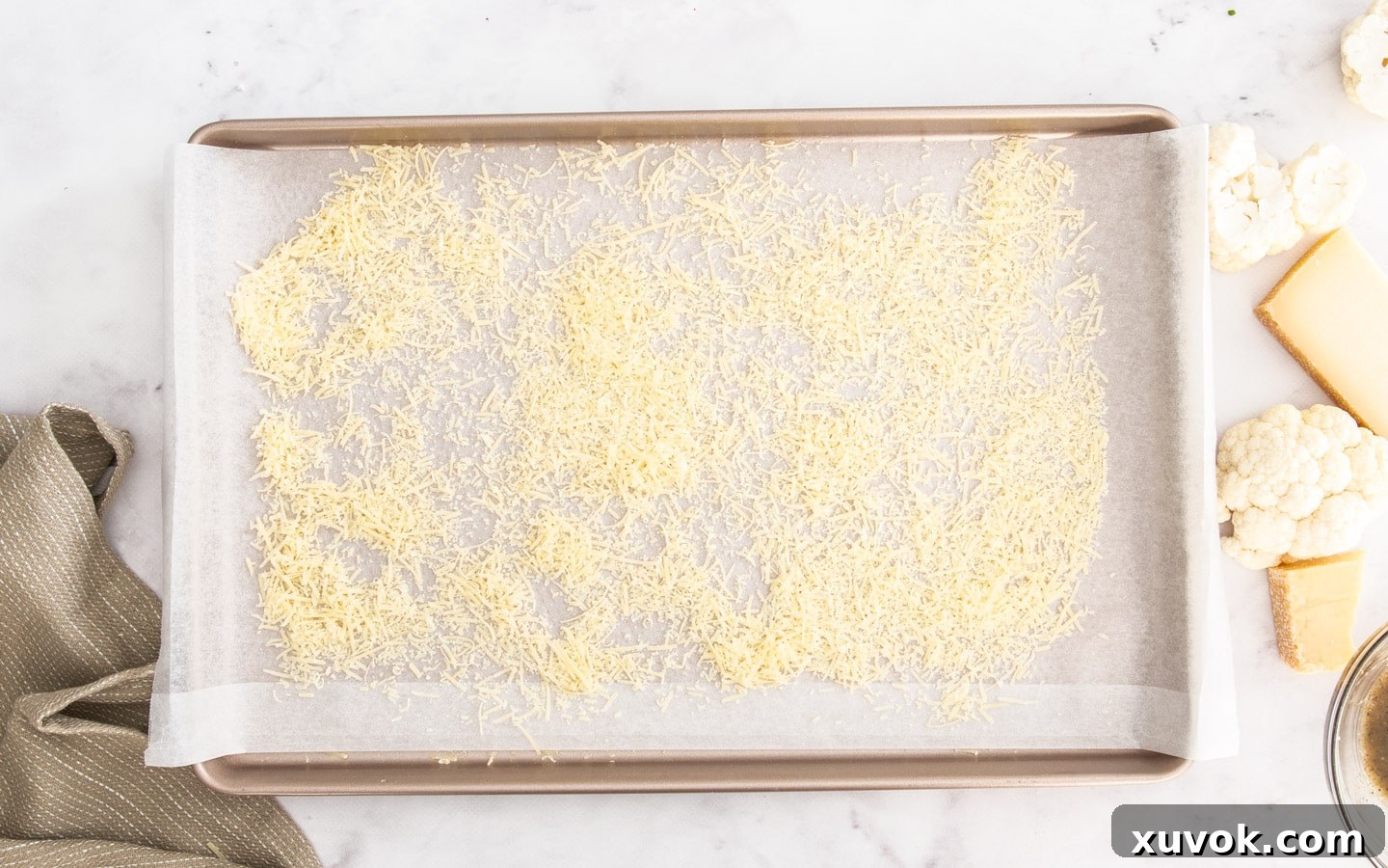 Finely grated Parmesan cheese evenly scattered over a baking sheet, creating a base for the cauliflower.