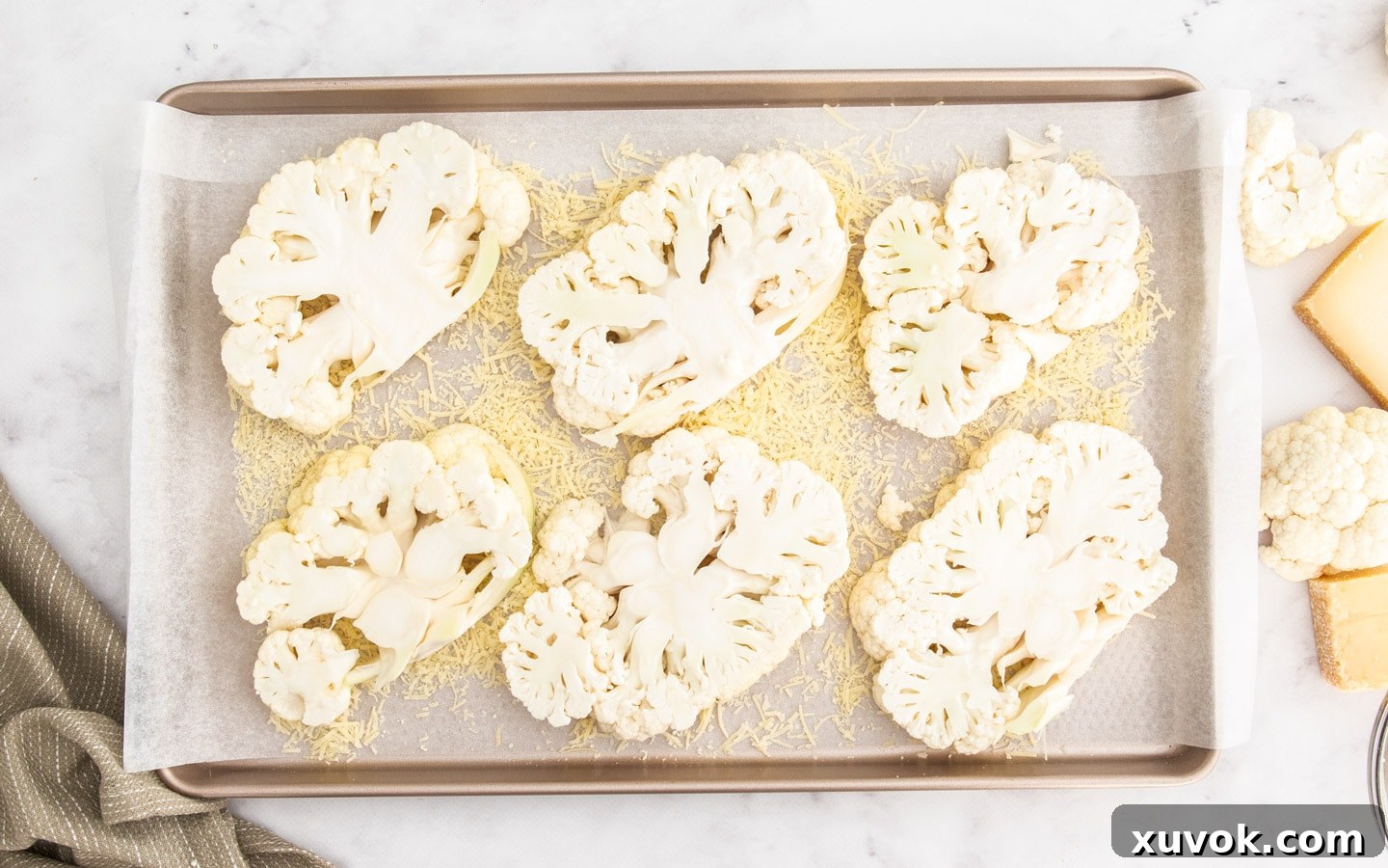 Six slices of cauliflower arranged on a baking tray, ready for seasoning and baking.