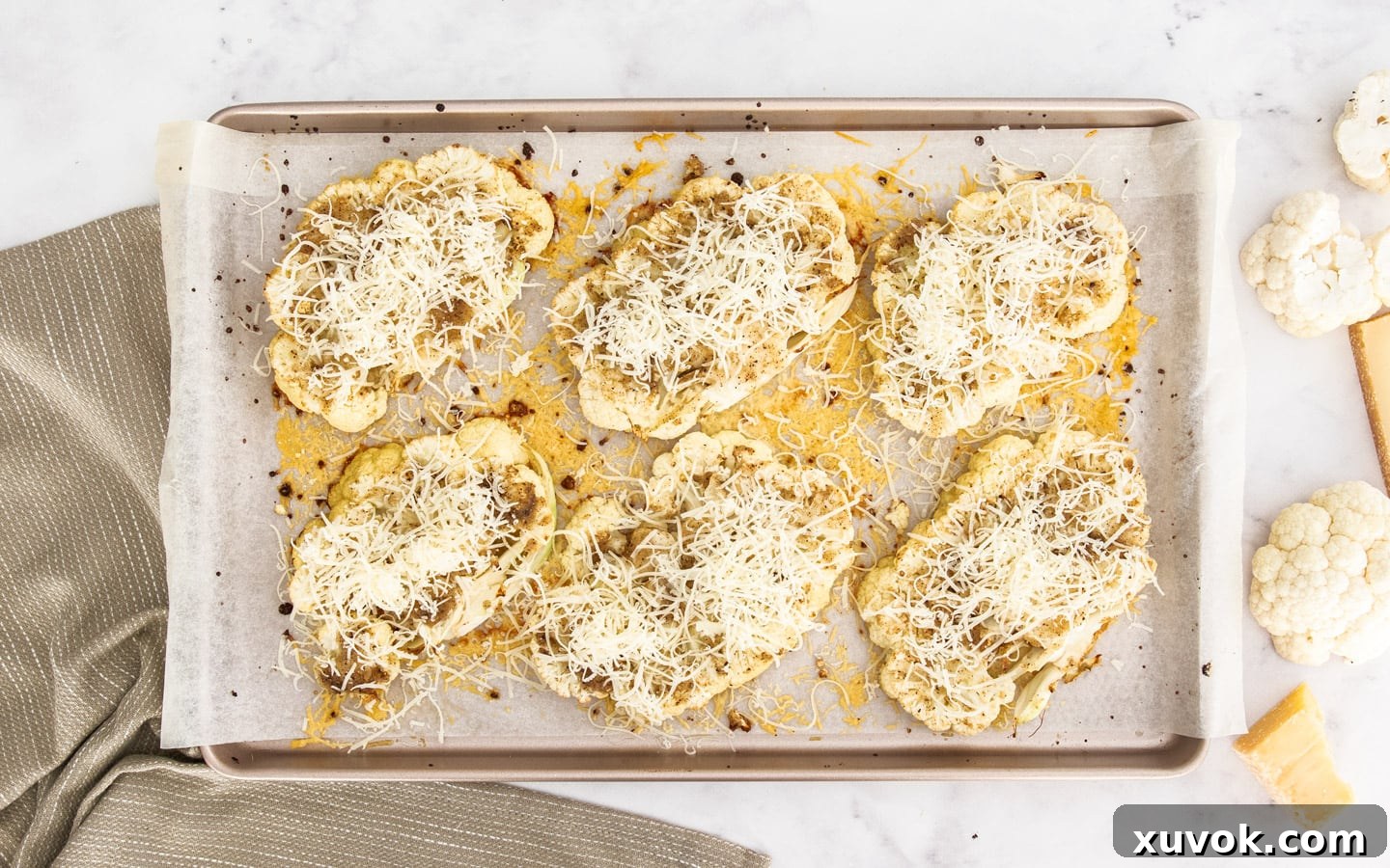 Roasted cauliflower steaks topped with a generous layer of Gruyère cheese, bubbling and golden, on a baking sheet.