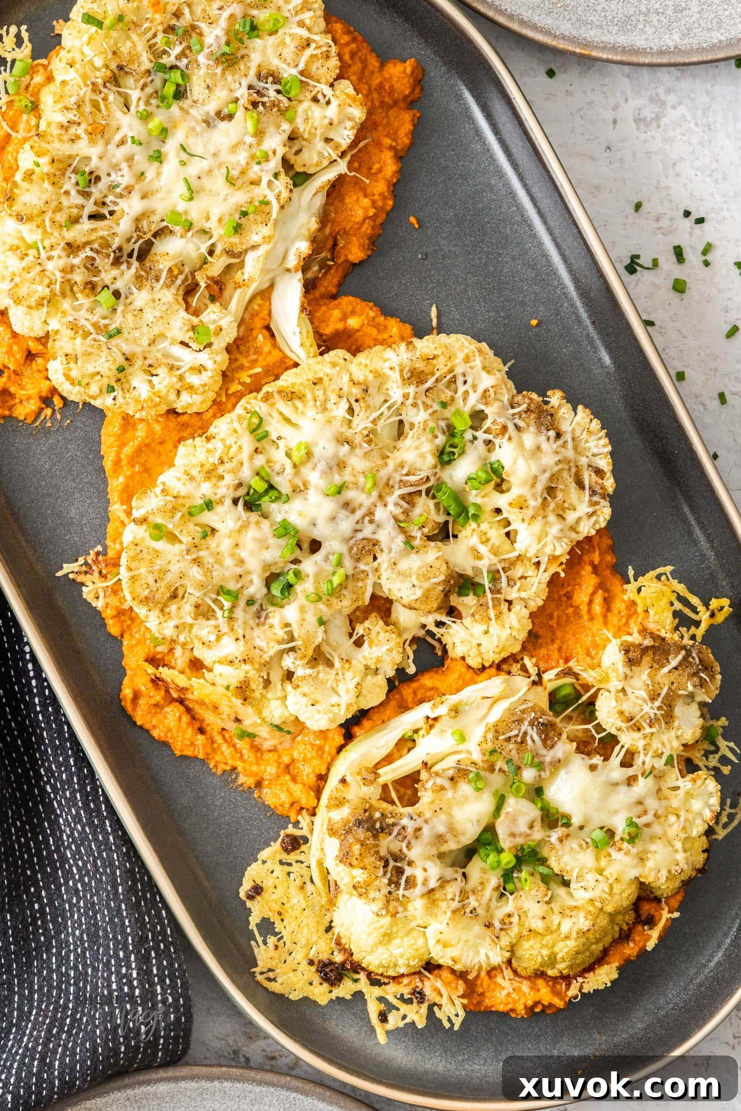 Cheesy cauliflower steaks served on a bed of vibrant romesco sauce, garnished with fresh herbs.