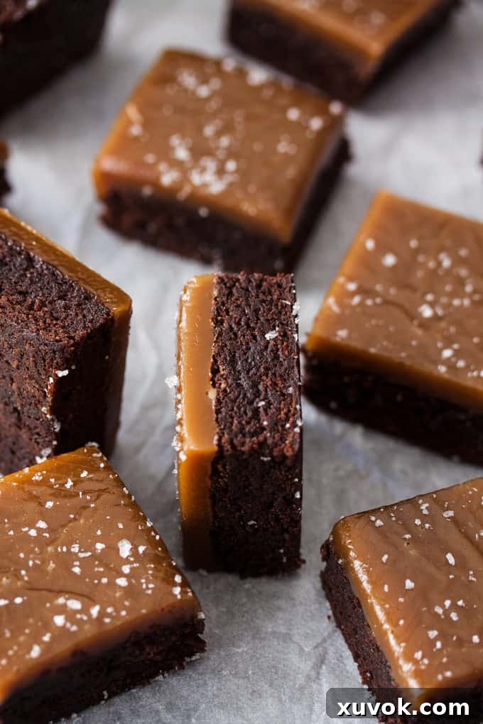 A batch of brownies, each topped with chewy caramel and sea salt flakes on a sheet of baking paper.