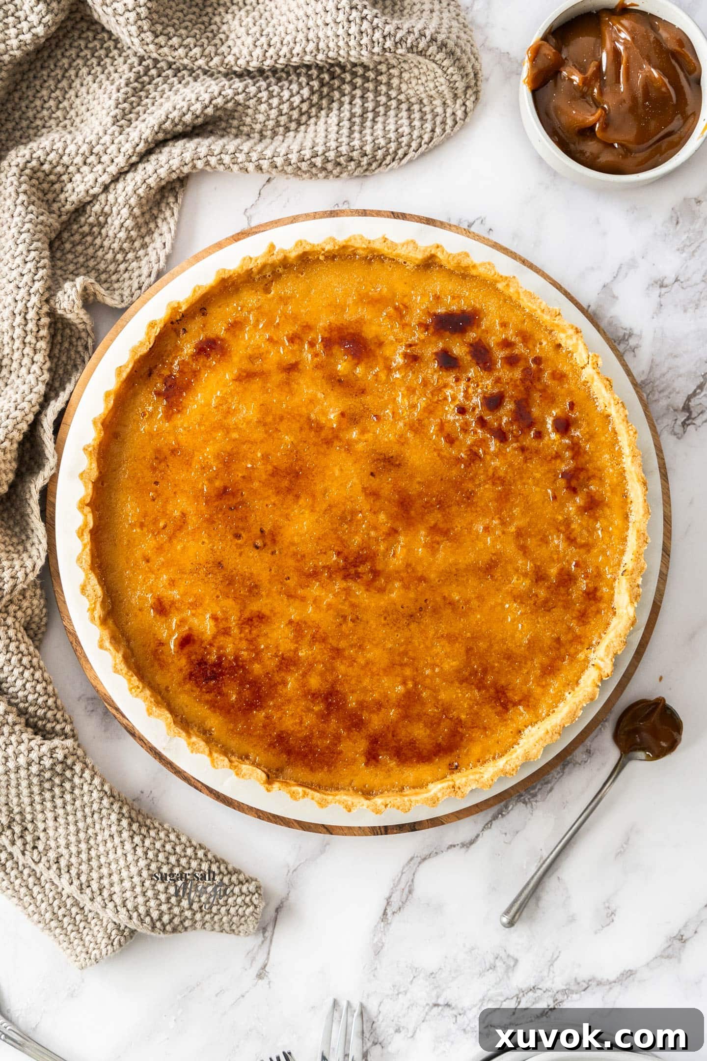 Top down view of the caramel creme brulee tart with a pot of caramel next to it, showcasing its golden crackable top and inviting texture.