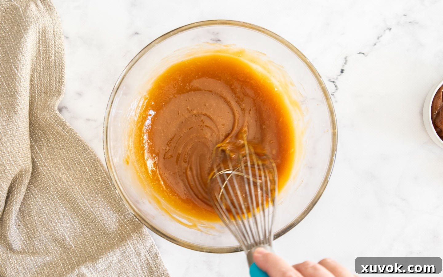 Whisking together caramel and eggs in a bowl, showing the creamy texture.