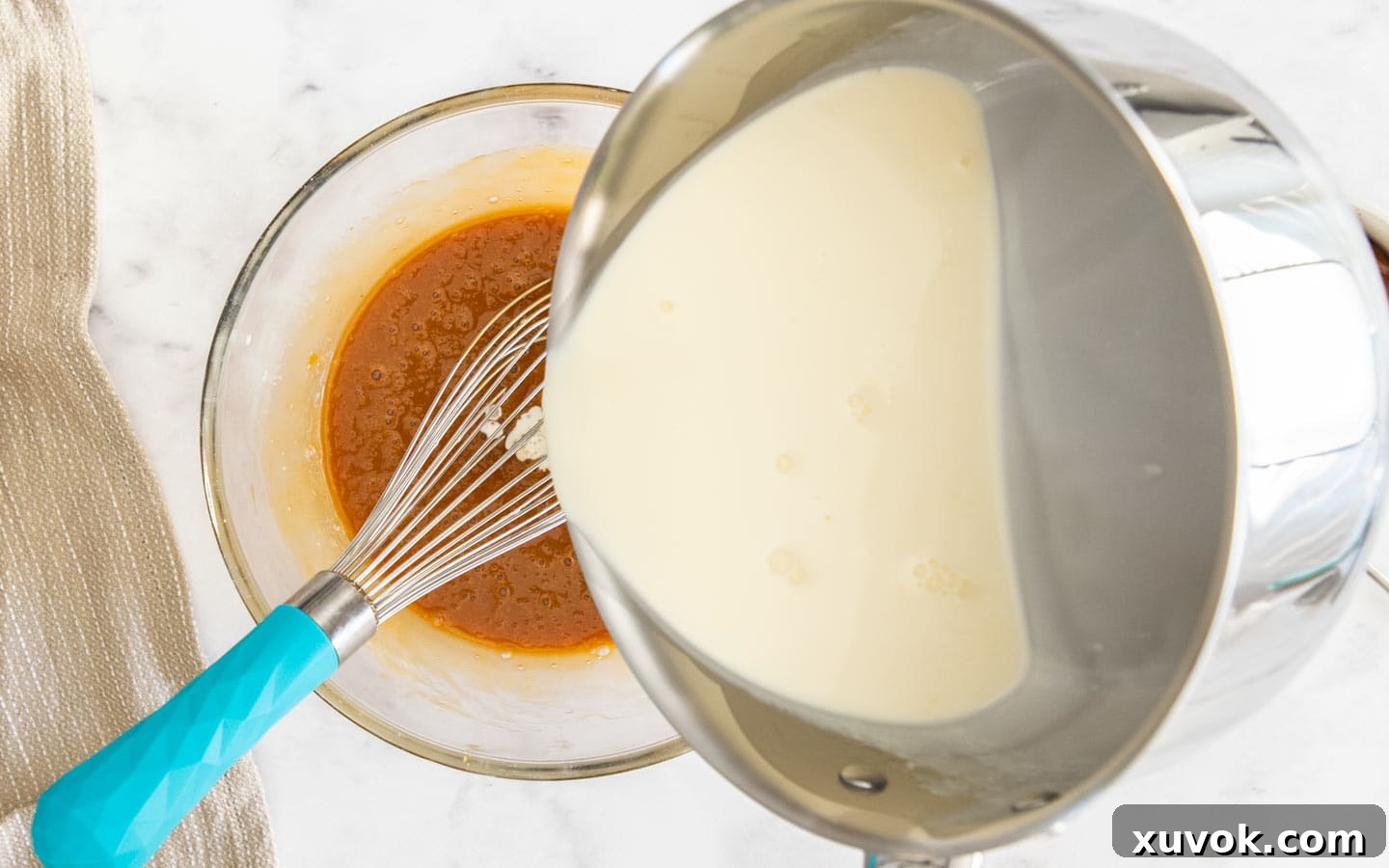 Slowly adding hot cream to the caramel and egg mixture while whisking, illustrating the tempering process.