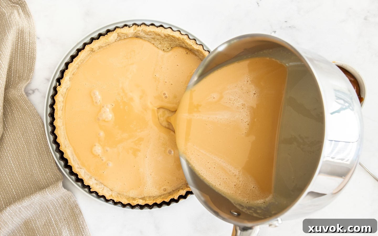 Pouring the caramel custard filling into the blind-baked tart shell.