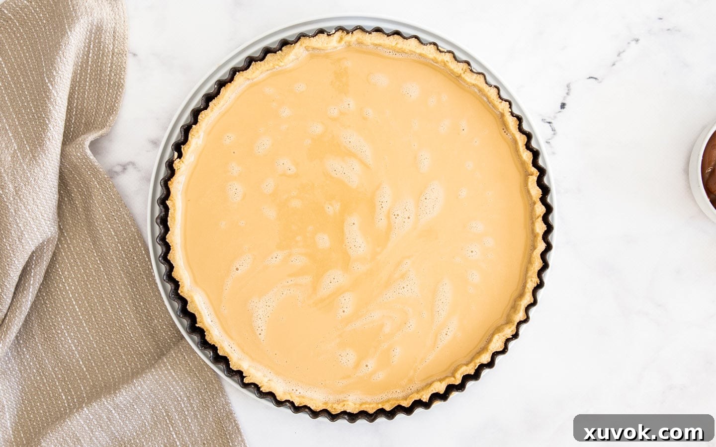 The caramel filling in the tart shell, perfectly prepared and ready to bake, showing a smooth surface.