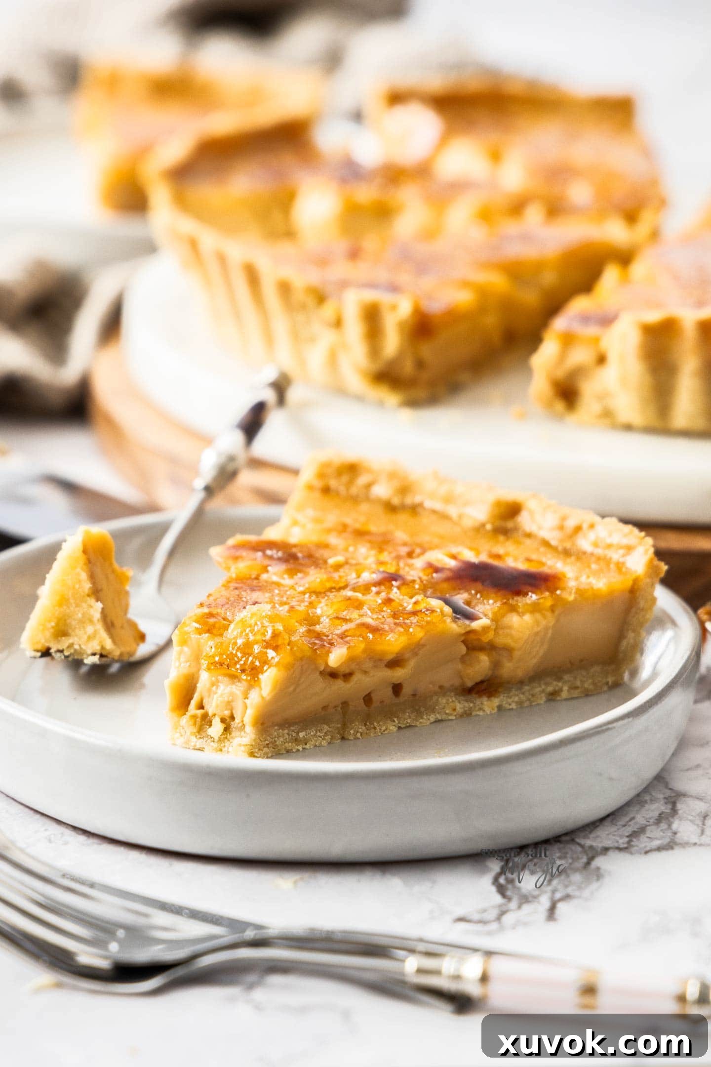 A slice of creme brulee tart with a forkful removed, showing the creamy interior and perfect crust.