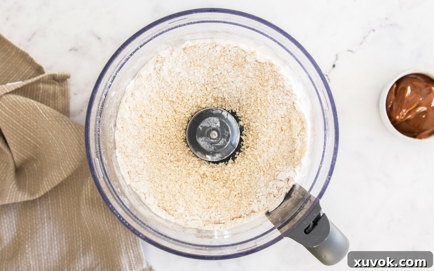 The pastry mixture in the food processor after the egg is added, showing a crumbly texture.