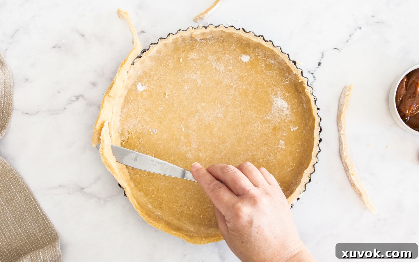 Cutting the overhanging pastry away from the tart shell with a knife, creating a clean edge.