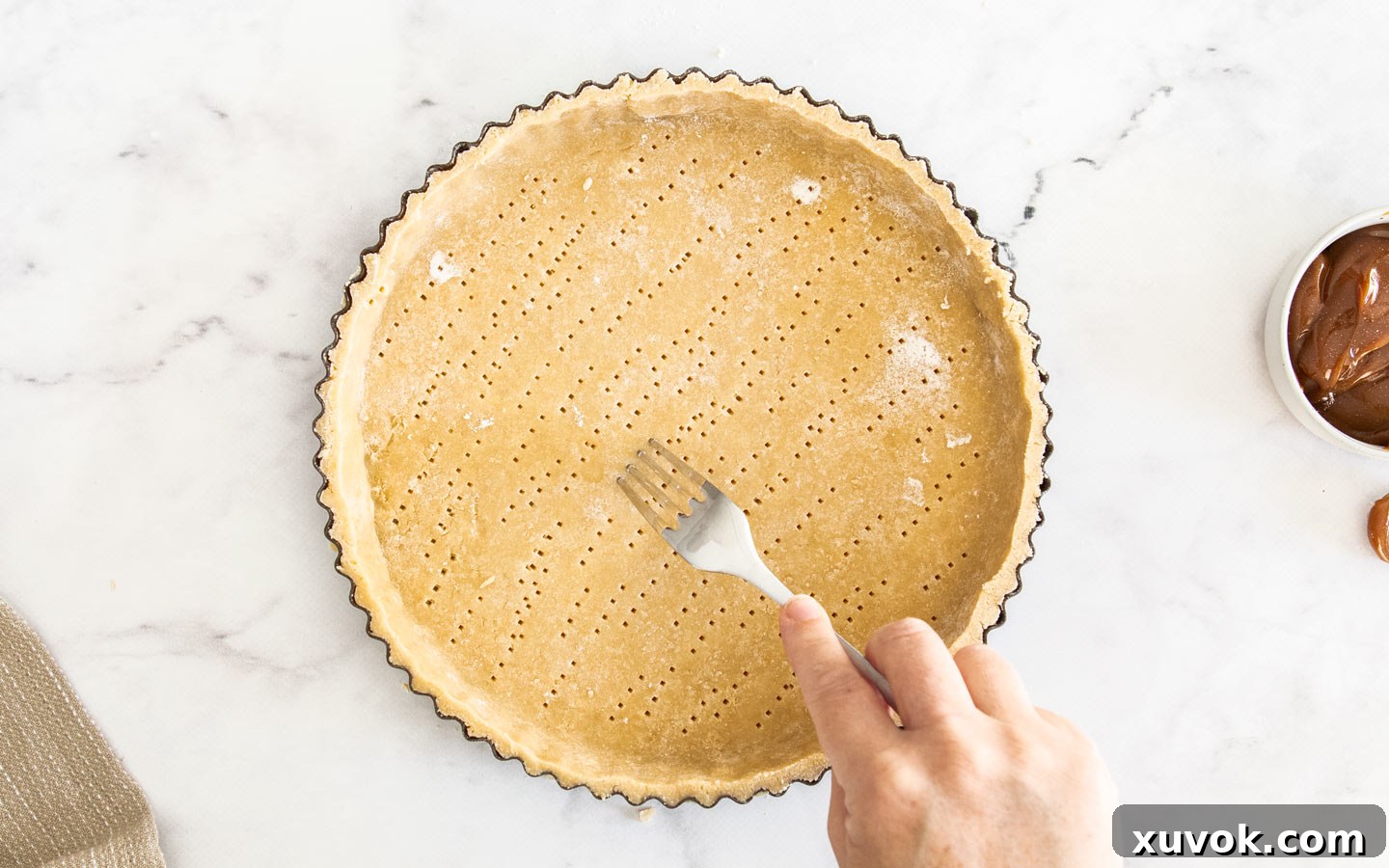 A hand using a fork to dock the tart shell base, showing multiple small holes.