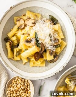 Top down view of the pasta in a bowl with a small bowl of pine nuts next to it.