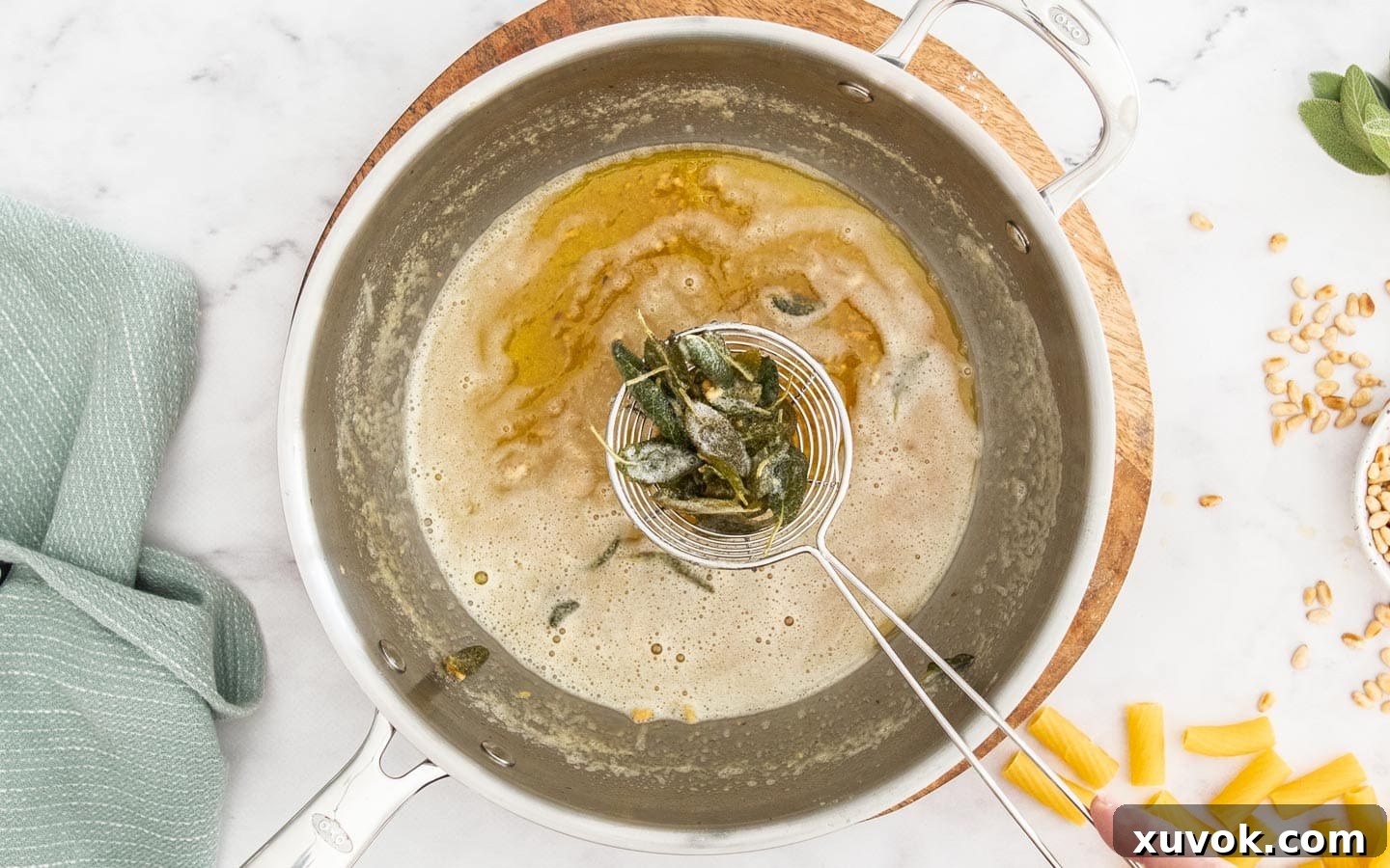 A slotted spoon gently scooping crispy, browned sage leaves out of the amber-colored brown butter in a hot pan.
