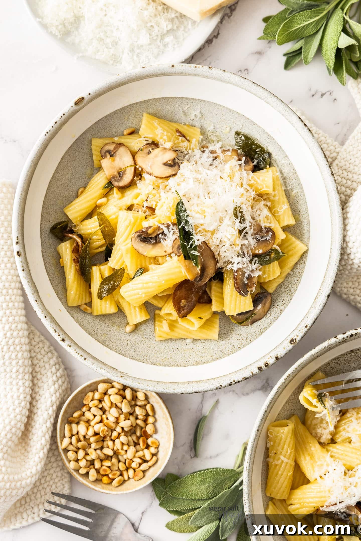 Two elegantly plated bowls of sage butter pasta, served alongside a small pinch bowl filled with toasted pine nuts, highlighting the dish's irresistible appeal.