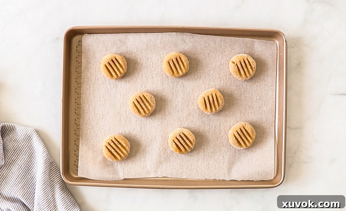 Balls of classic peanut butter cookie dough on a baking sheet, pressed with a fork to create a criss-cross pattern on top.