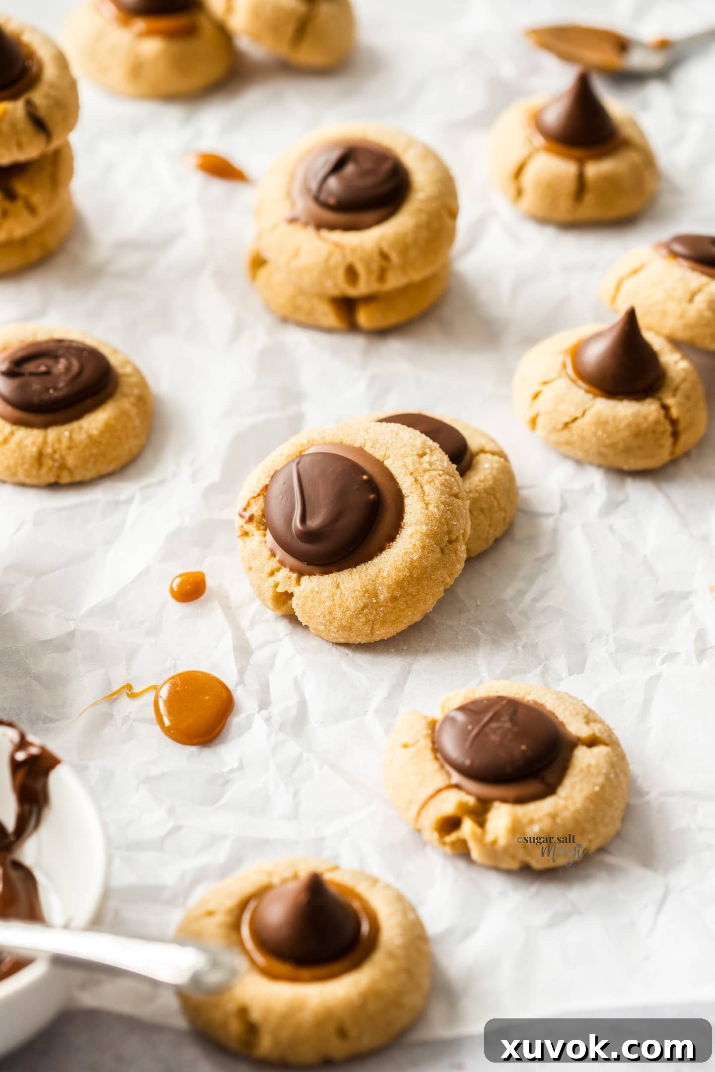 A batch of freshly baked caramel peanut butter thumbprint cookies on a sheet of baking paper, ready to be enjoyed.