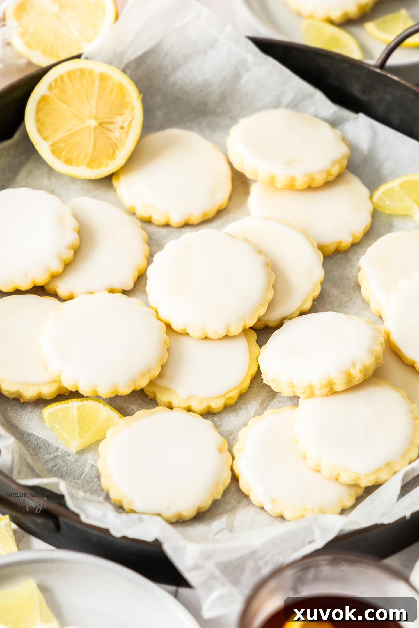A generous batch of glossy, iced lemon cookies piled artfully on a white serving plate, highlighting their bright glaze and inviting texture, ready to be enjoyed.
