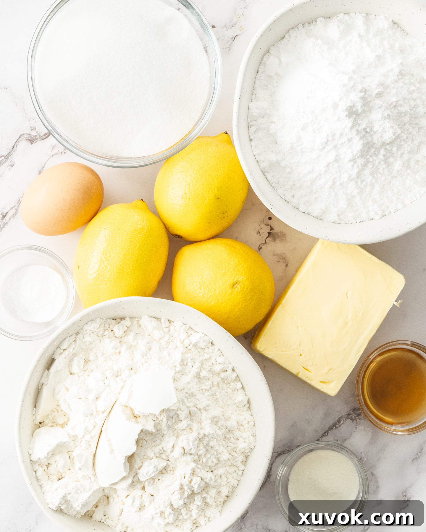 Essential ingredients for baking lemon sugar cookies, including fresh lemons, butter, sugar, flour, and eggs, artfully arranged on a pristine marble surface, ready for preparation.