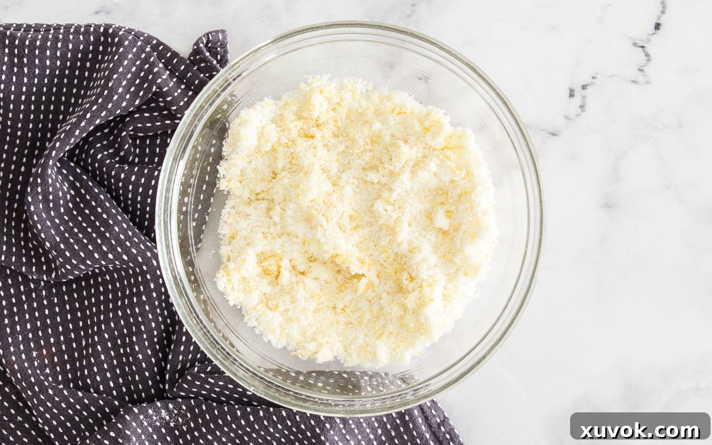 Close-up of lemon zest being rubbed into sugar by fingertips in a bowl, creating a fragrant, 'wet sand' texture that signifies deep lemon infusion for baking.