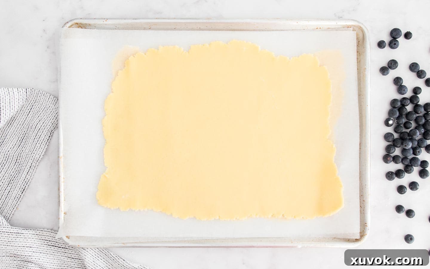 Two rolled out pastry rectangles stacked on a baking tray, separated by parchment paper and ready for chilling.