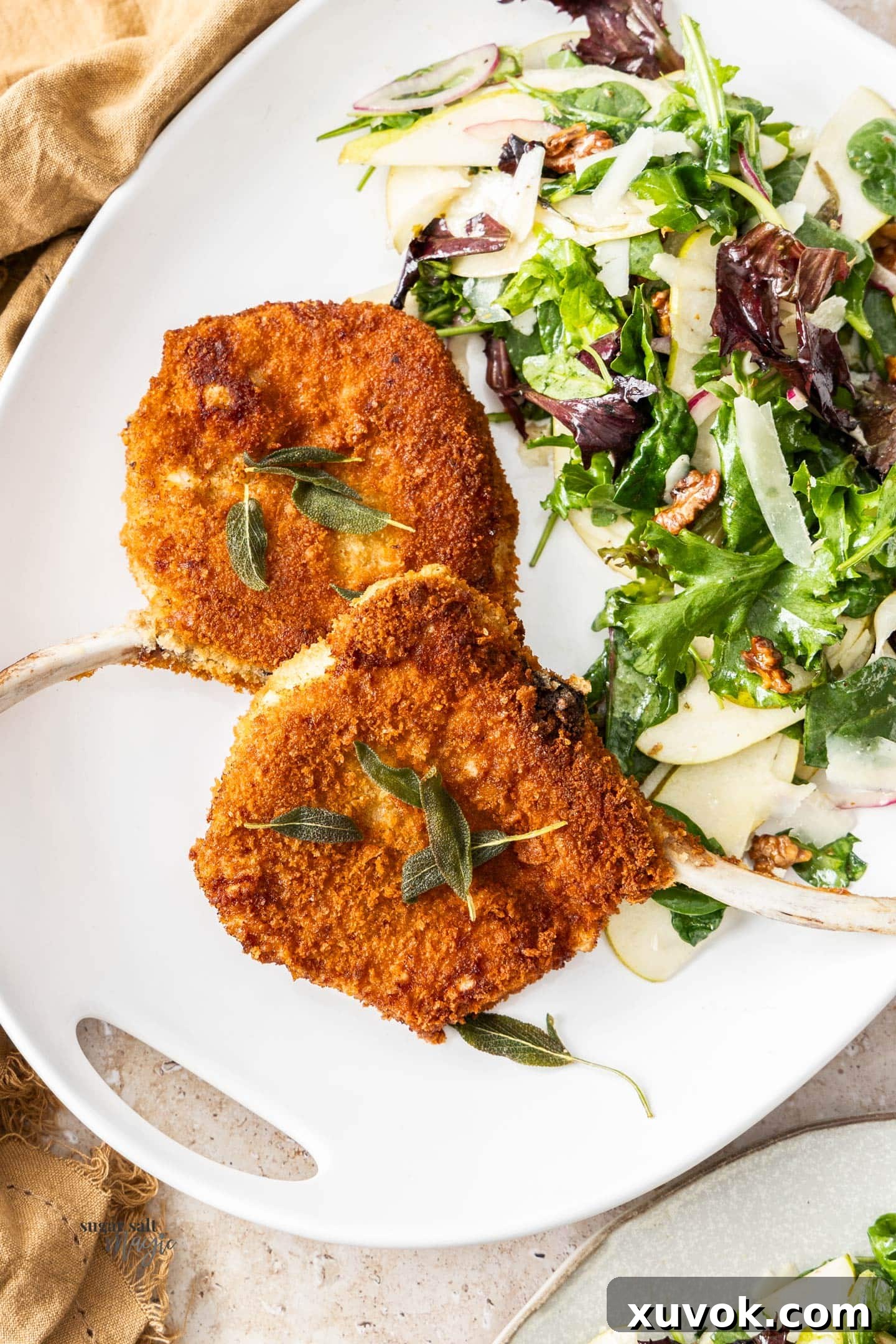 Two golden-brown pork Cotoletta Milanese cutlets on a serving platter with a fresh salad beside them, showcasing their crispy texture.