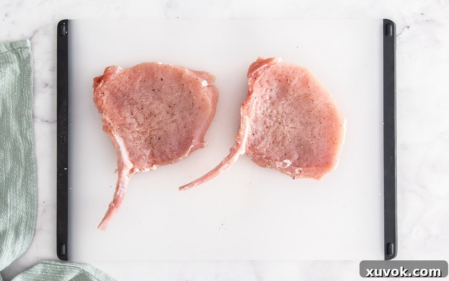 Two raw pork cutlets, flattened and seasoned, on a chopping board ready for breading.