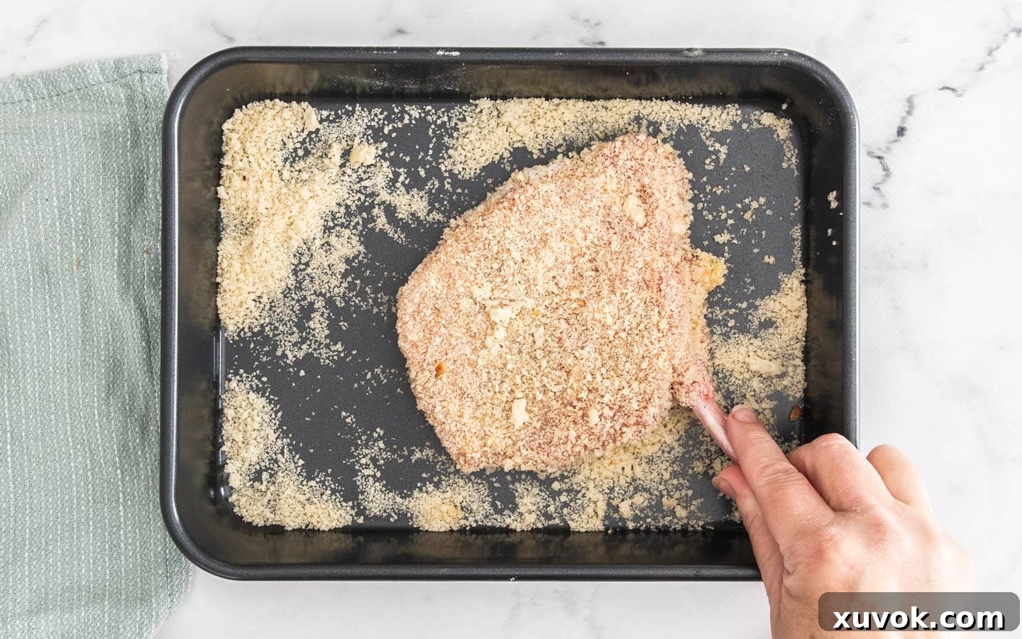 A pork cutlet being pressed into a bowl of fine breadcrumbs, showing the final step of the breading process.