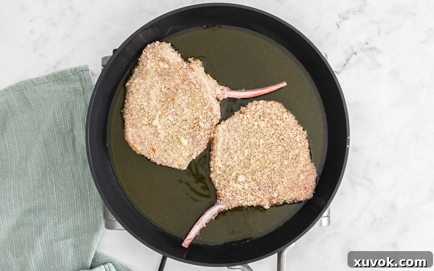 Two breaded pork cutlets being carefully placed into a hot frying pan with clarified butter, starting the cooking process.