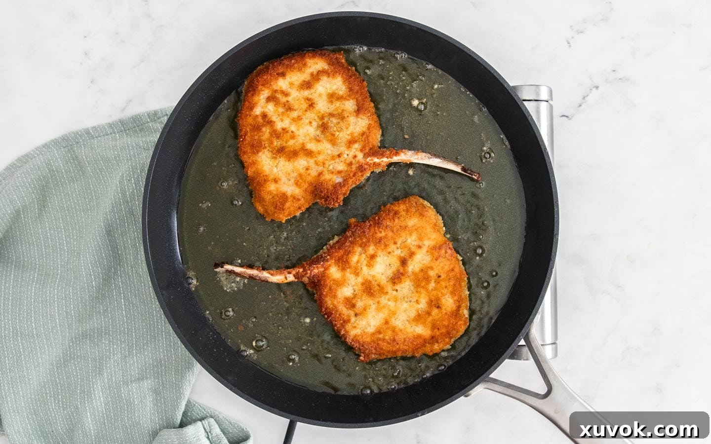 Two pork cotoletta cutlets frying in a pan, showing a perfectly golden-brown and crispy breading.
