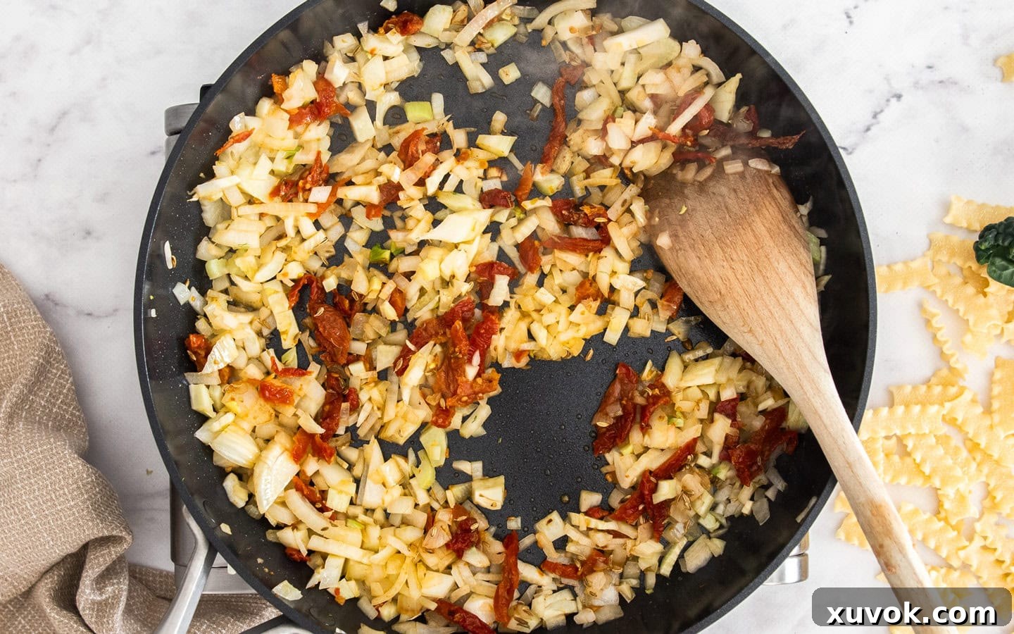 Diced onion, fennel, and sliced sun-dried tomatoes softening in a pan, forming the aromatic base for the pasta sauce.