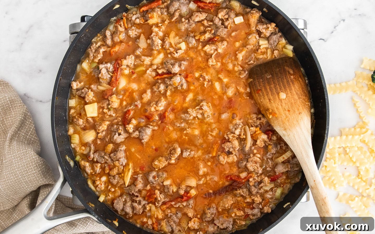 The pan after chicken stock and tomato paste have been added to the browned sausage and vegetables, simmering to thicken.