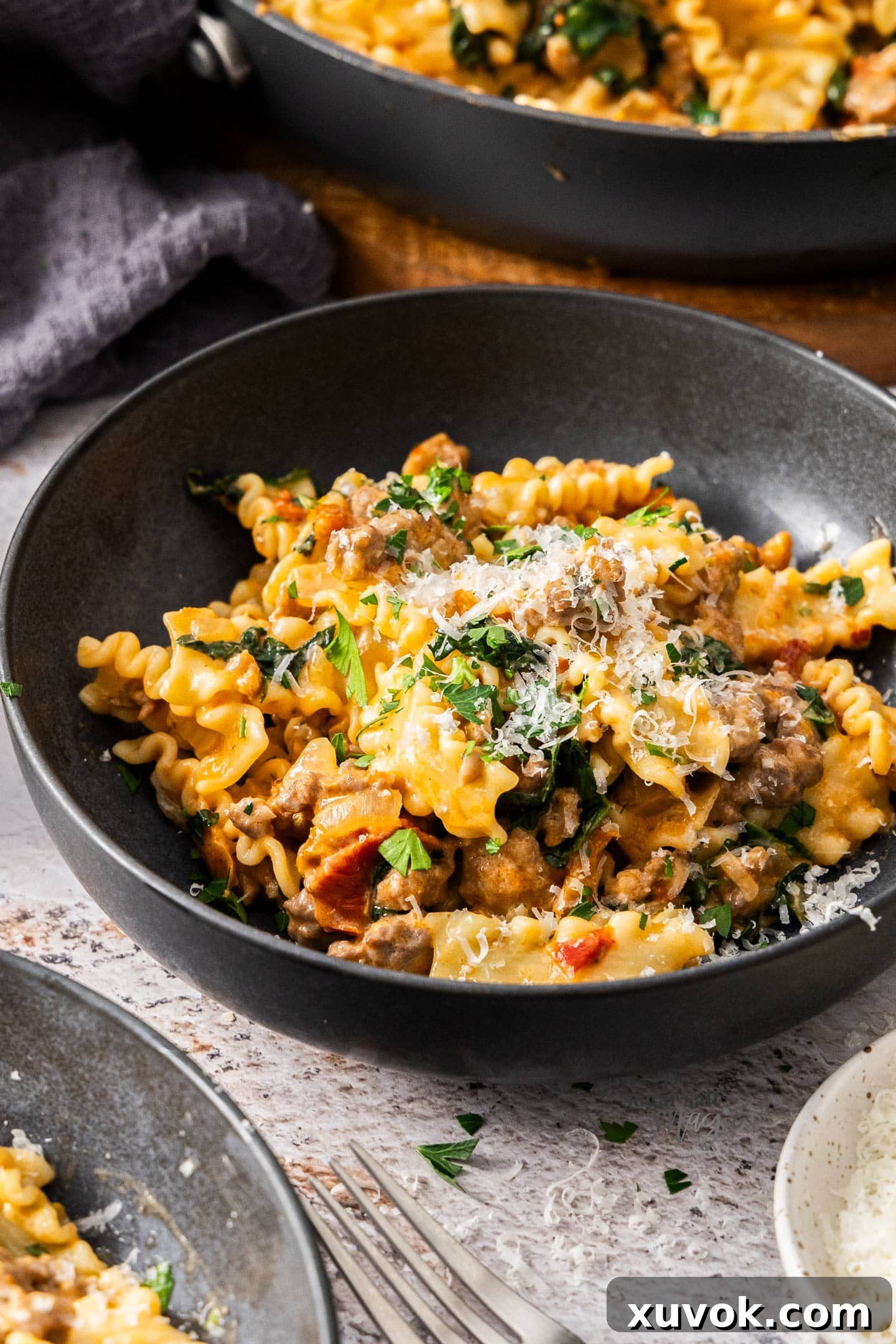 A pasta bowl filled with creamy fennel sausage pasta, generously topped with freshly grated Parmesan cheese and a sprig of fresh parsley.