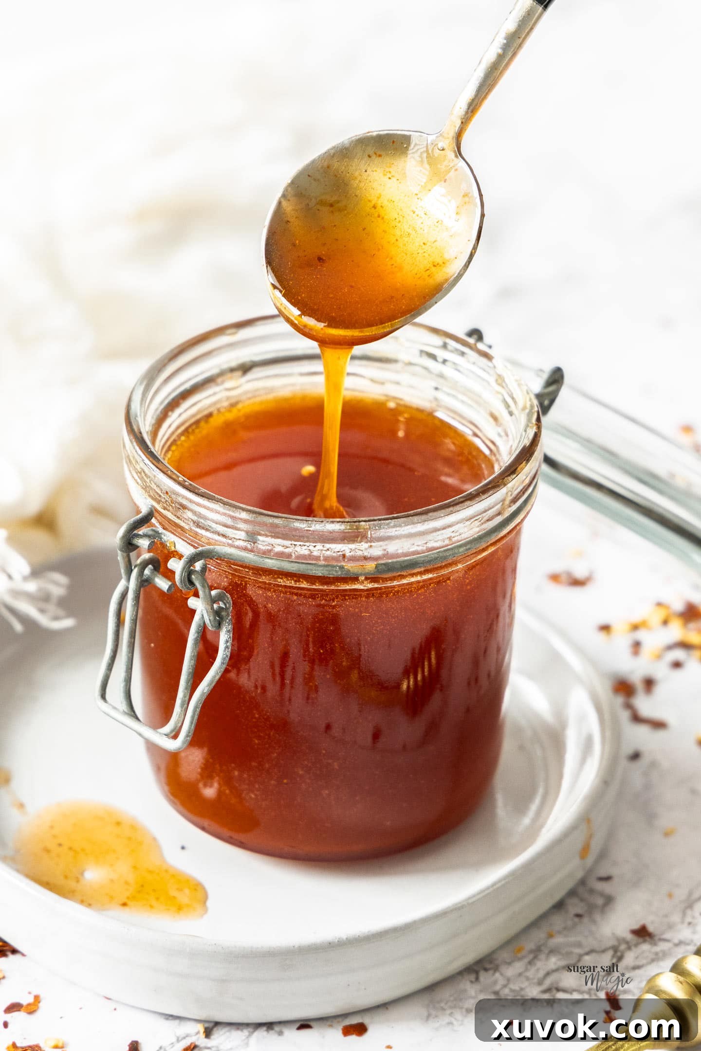 A spoon drizzling hot honey into a jar.