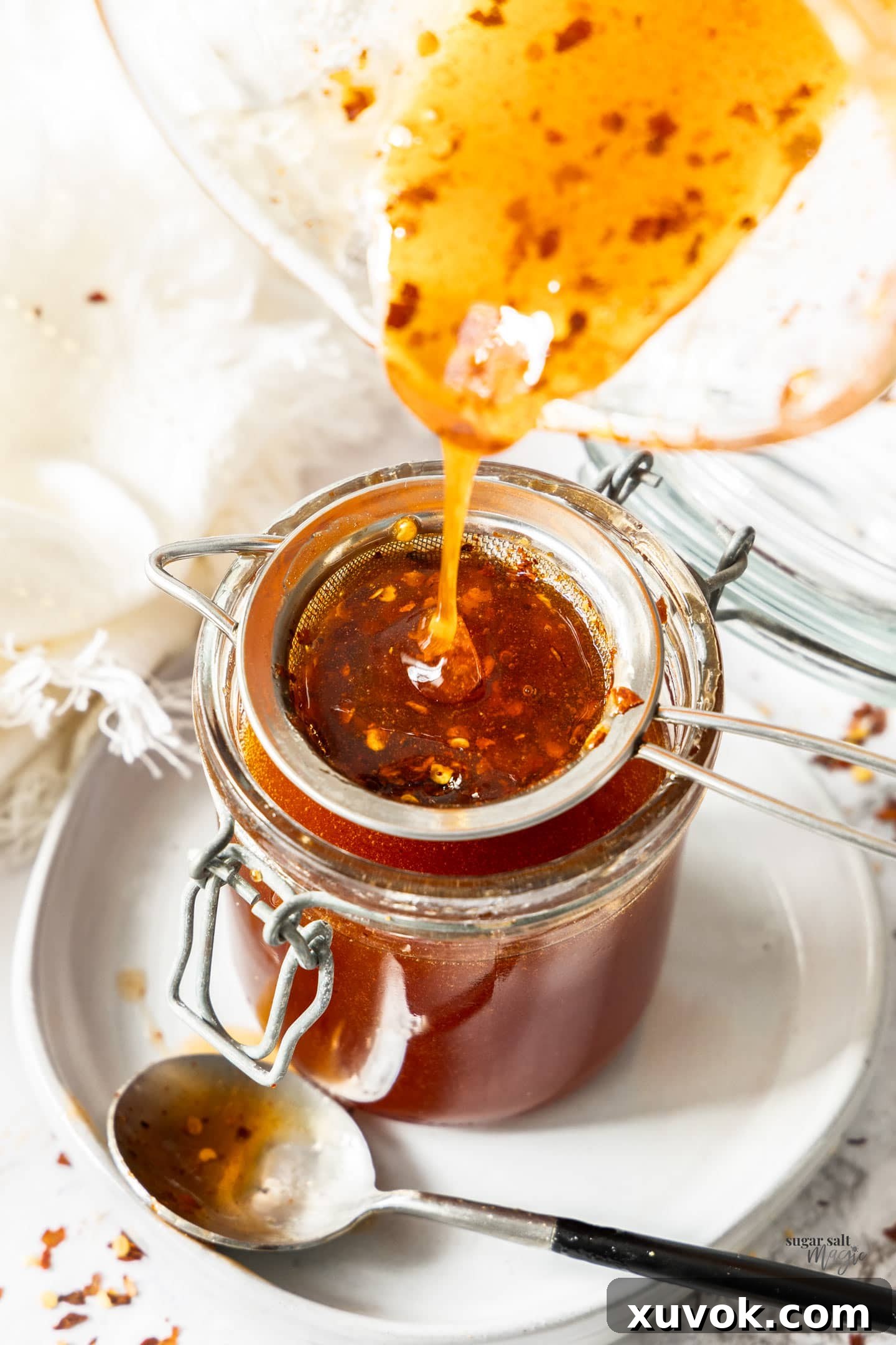 The hot honey being poured through a strainer into a jar.