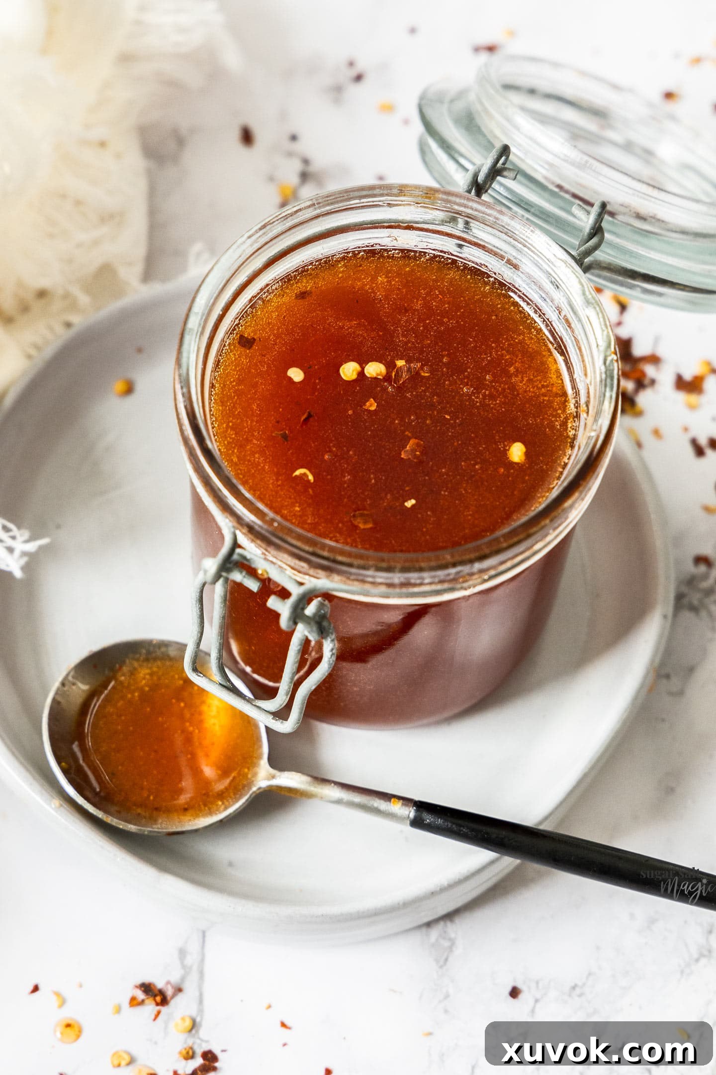 A glass jar filled with hot honey with chilli flakes on top.