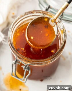 A spoon taking some hot honey out of a jar.