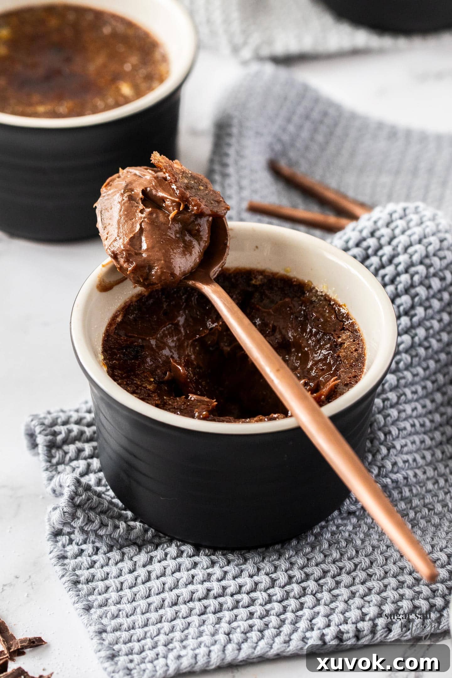 A spoon resting on the edge of a ramekin of chocolate crème brûlée, showcasing the creamy texture and rich color.