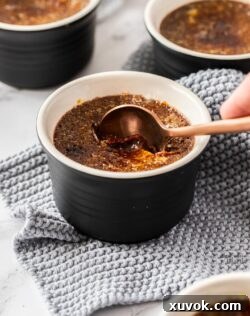 A spoon cracking the sugar top of a chocolate crème brûlée, revealing the creamy interior.