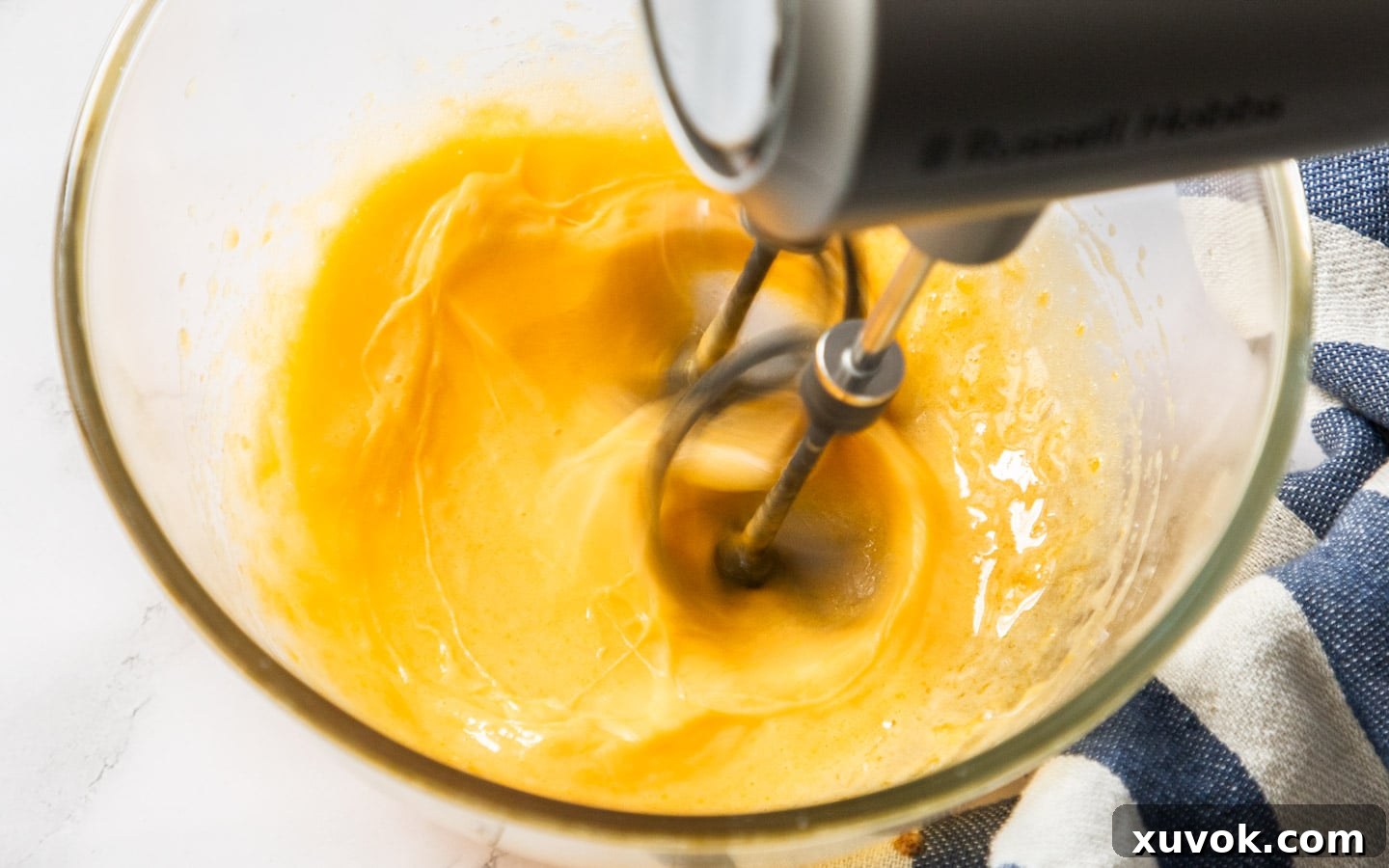 Egg yolks being whisked with sugar until pale and creamy, preparing them for tempering.