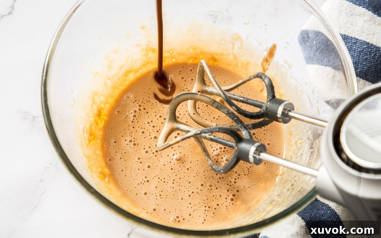 Slowly pouring the warm chocolate cream into the whisked egg yolks, tempering the mixture to create the custard.