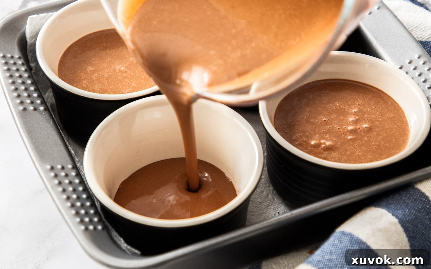 Smooth chocolate custard being poured into individual ramekins, ready for the water bath and baking.