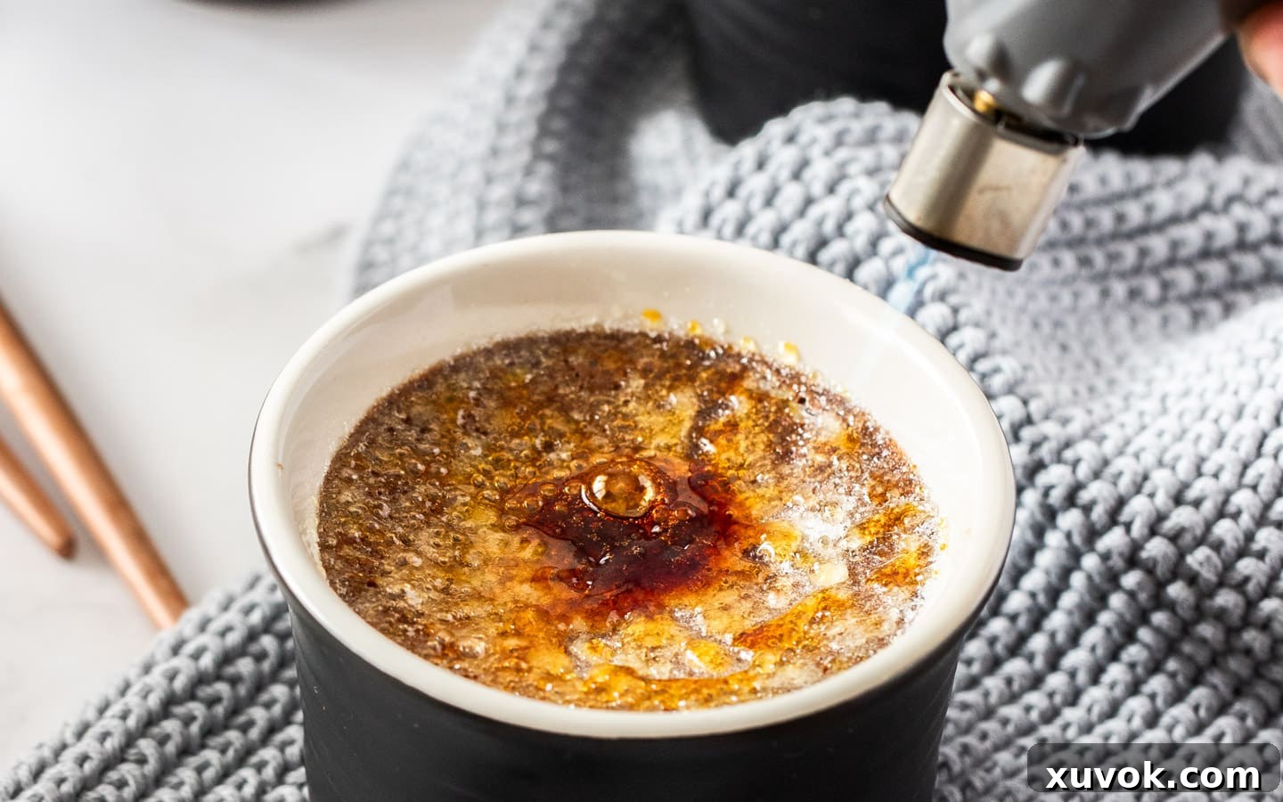 A kitchen torch being used to caramelize the sugar topping on a chocolate crème brûlée, creating a golden, crunchy crust.