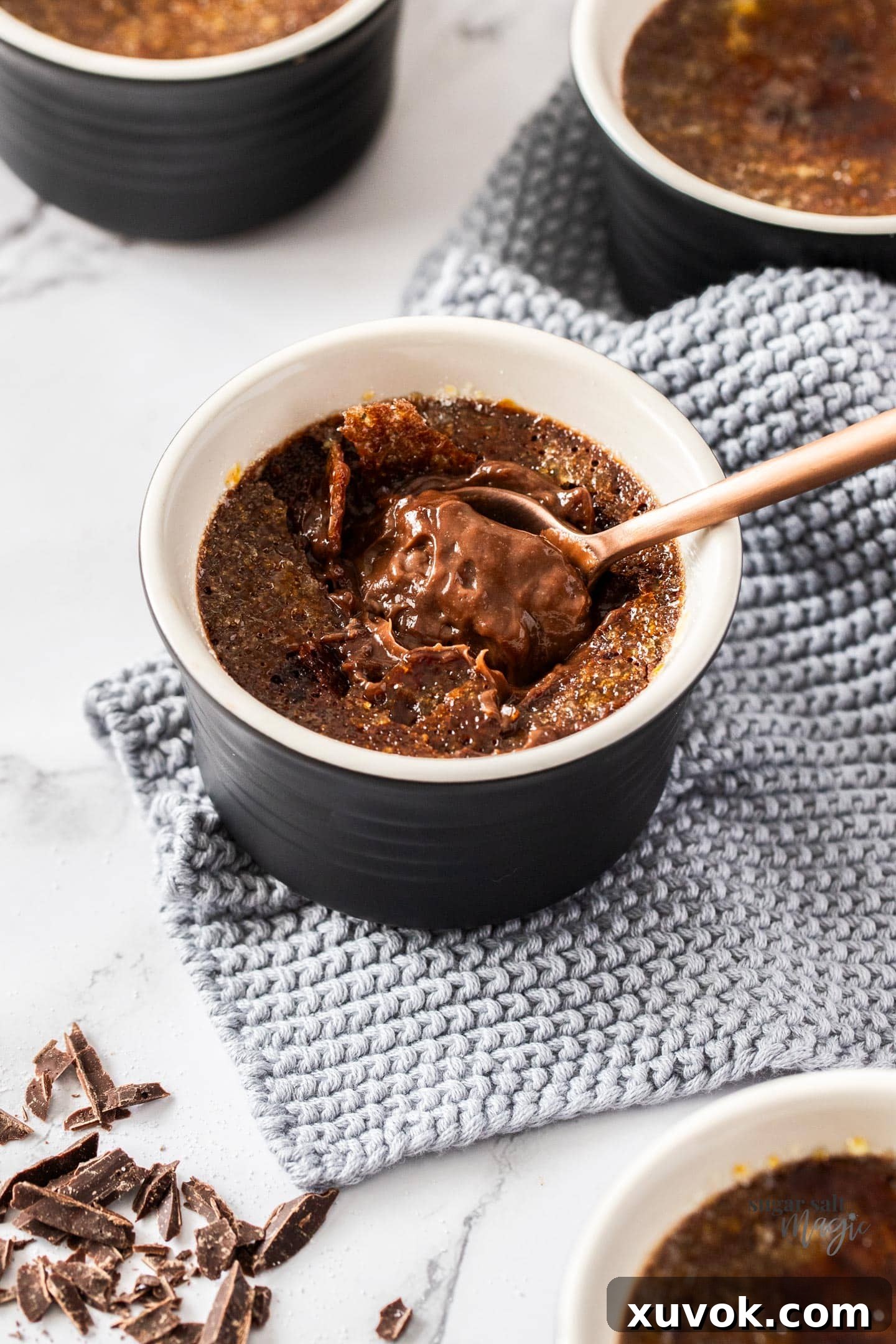 A spoon breaking through the crunchy caramelized sugar top of a chocolate crème brûlée, revealing the creamy custard beneath.