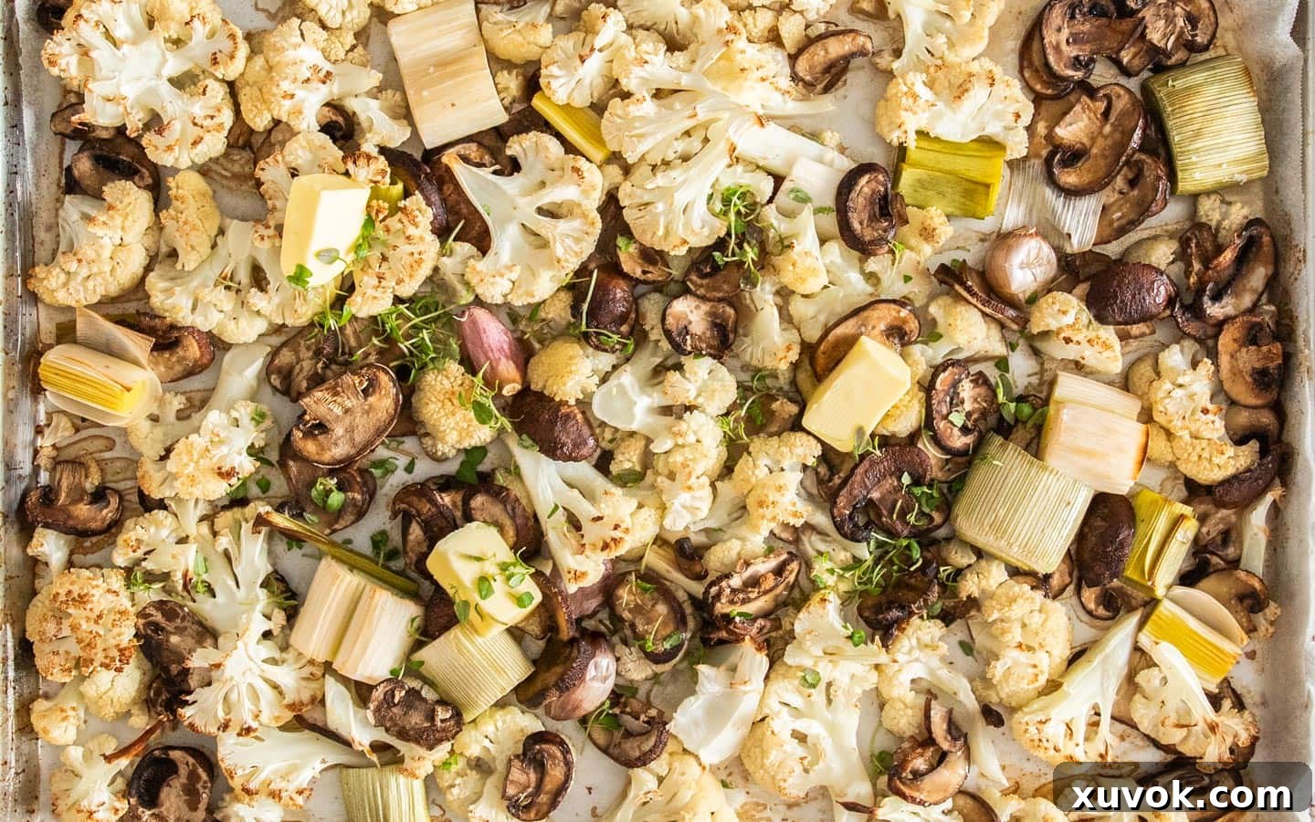 The roasted vegetables on a baking pan, showing golden-brown caramelization, with butter and fresh thyme added.